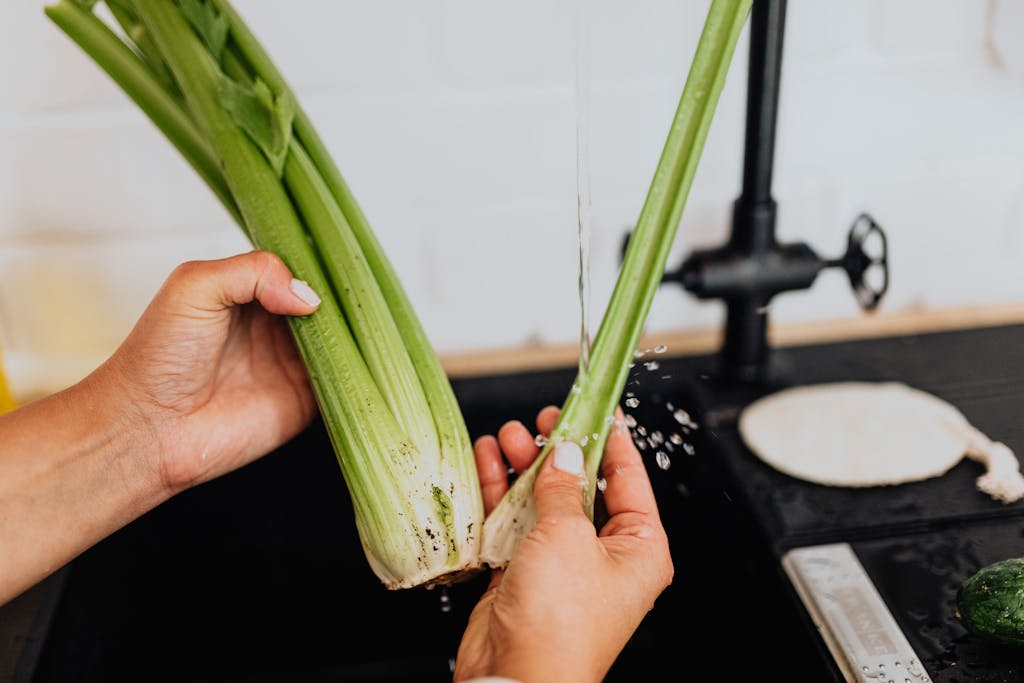 Close-up of a woman washing fresh celery in a kitchen sink, promoting healthy eating.